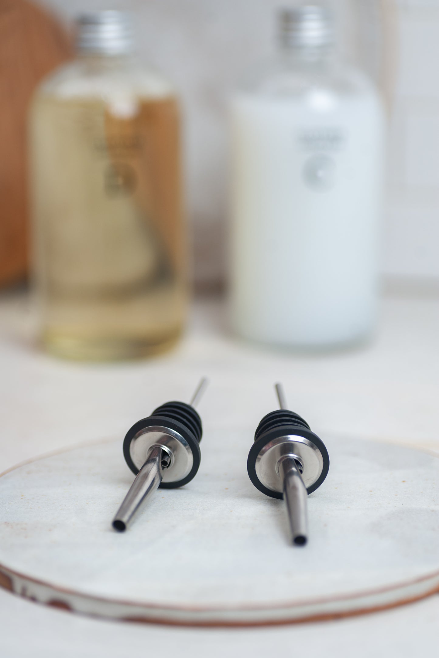 Two bottle nozzles on a ceramic plate with bottles in the background