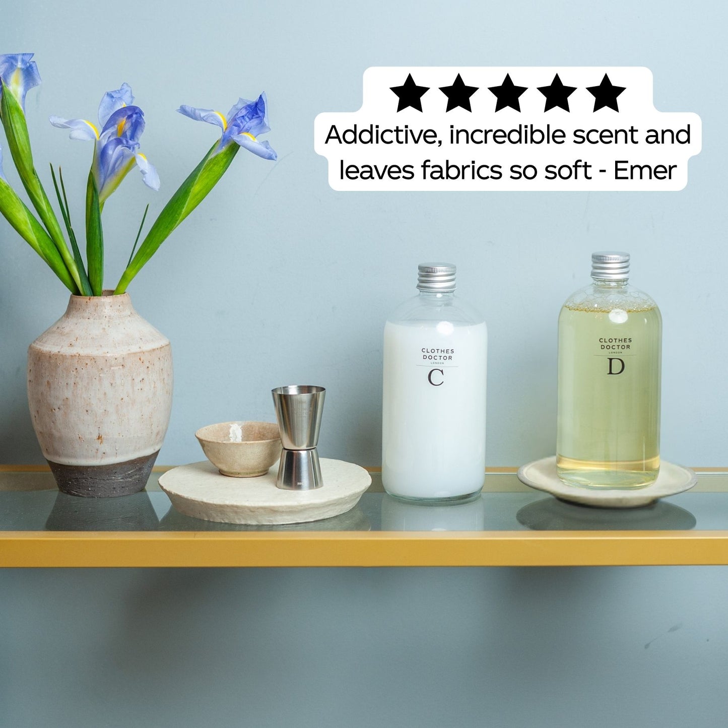 Two bottles on a shelf with a vase of flowers and decorative items against a light blue wall.